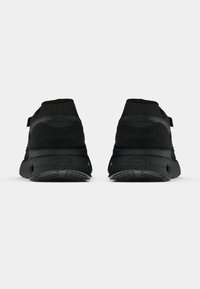 Um par de tênis Reebok pretos visto de trás em um fundo branco liso, destacando o design do calcanhar e da sola.