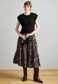 Czarny dzianinowy top bez rękawów, warstwowa czarna spódnica w kwiaty z różowymi i zielonymi wzorami, czarna kopertówka oraz brązowe kowbojskie botki na obcasie.