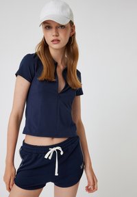 Donkerblauwe T-shirt met korte mouwen en een ritssluiting bij de hals, gecombineerd met donkerblauwe shorts met trekkoord. Witte accenten op de shorts. Gladde katoenstof.