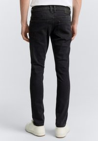 Jeans de denim negros con un corte ajustado, que cuentan con dos bolsillos traseros y sutiles detalles de costura. Combinados con zapatillas blancas.