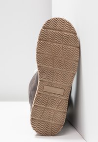 Chaussure en daim marron avec une semelle en caoutchouc. La semelle présente un motif en zigzag et un logo de la marque, taille 37 embossée sur le côté.