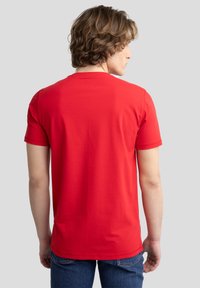 Raudona trumpomis rankovėmis medvilninė T-shirt marškinėliai su apvalia iškirpte. Minkšta tekstūra, glotni danga ir minimalus dizainas be matomų logotipų ar raštų.