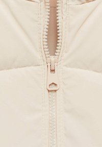 Chaqueta de plumas color beige claro con cremallera y un tirador de plástico, que presenta una tela texturizada, costuras en contraste y un interior forrado.