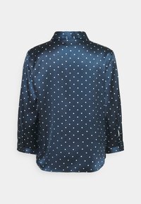 Camicia di raso blu navy con pois bianchi, maniche lunghe e polsini con bottoni. Design del colletto con una texture liscia.
