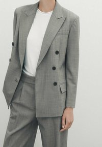 Blazer doppiopetto grigio chiaro con un motivo testurizzato, bottoni neri e una tasca sul petto, abbinato a una t-shirt bianca a girocollo.