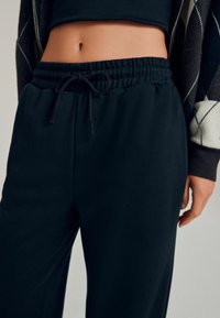 Svart sweatpants med elastisk talje og justerbar snor. Fremstillet af blødt stof med en glat tekstur og afslappet pasform.