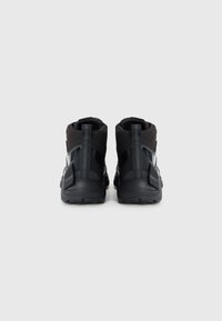 Zapatillas altas negras con parte superior de malla, acentos suaves y suelas de goma texturizadas. Presenta un talón reforzado y un detalle de logo.