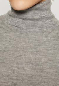 Gråribbete høyhalset genser med høy krage, teksturert overflate og en tettsittende fasong. Stoffet ser mykt og fleksibelt ut.