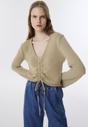 Beige gestrickter Pullover mit V-Ausschnitt, ausgestattet mit einem gerafften Design und Kordeln an der Taille. Akzentuiert mit Kordel-Details in der Mitte.