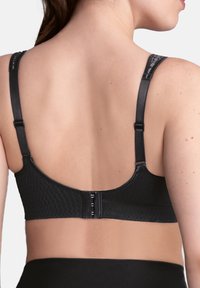 Zwarte bh met textiel, verstelbare schouderbanden en een haaksluiting aan de achterkant. Heeft een naadloos ontwerp en een gladde afwerking.
