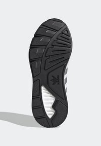 Svart gummi sneaker-sula med strukturerat grepp, med en vit mellansula och tre vita randdesign. Adidas-logotyp prägling.