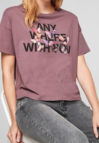 Krátký rukáv, mauve tričko s volným střihem, s černým textem a barevnou grafikou motýlů na přední straně.