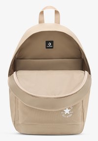 Beežimad värvi lõuendist seljakott ümara ülaosaga, ees oleva klapi ja logomärgiga. Omadusteks on avar sisu ja sile tekstuur.