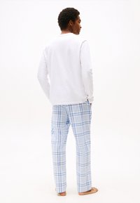 Hvid langærmet top med rund halsudskæring, parret med blå ternede pyjamasbukser, der har et mønster med lyseblå og mørkeblå tern.