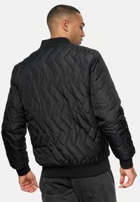 Svart quilted bomberjakke med et strukturert chevronmønster, ribbestrikkede mansjetter og hem, samt en strømlinjeformet, tettsittende silhuett.