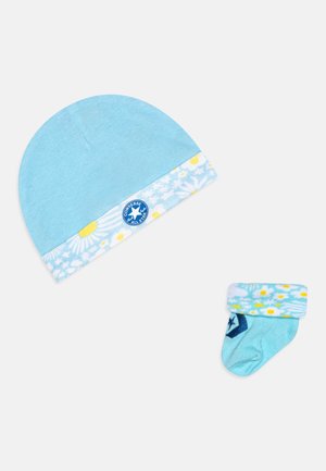 Beanie din bumbac albastru cu manșetă cu model de margarete și logo-ul Converse; ciorap în nuanță de albastru deschis, de dimensiune pentru bebeluși, cu un design floral similar.