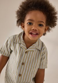 Camiseta de manga corta para niños en rayas verde pálido y amarillo, con cuello de solapa y cierre de botones de madera. Textura de tela suave.