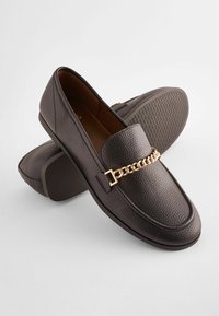 Dark brown loafers made of textured leather with a gold chain accent. Flat rubber sole with a patterned grip. Classic slip-on design.
