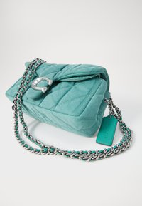Quilted teal fabric handbag with a silver chain strap, featuring a distinctive clasp and a green tag attached.