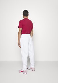 Camisa roja de manga corta combinada con pantalones deportivos blancos y zapatillas deportivas con acentos en rosa, vista desde atrás. Diseño simple y relajado.
