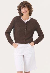 Brauner gerippter Cardigan mit einem runden Halsausschnitt, Knopfverschluss vorne und langen Ärmeln, kombiniert mit weißen Denim-Shorts.