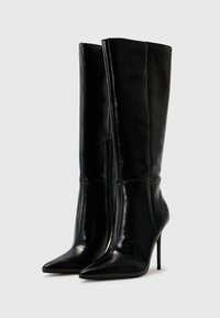 Bottes noires en cuir à talons hauts avec bouts pointus, design épuré, tige montant jusqu'au genou et détail de fermeture éclair sur le côté. Texture lisse et sans motifs visibles.