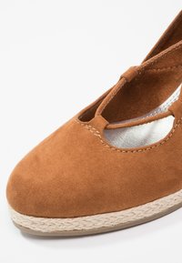 Espadrille en suède marron avec bout rond, design à T, et semelle en jute tissée sur fond blanc.