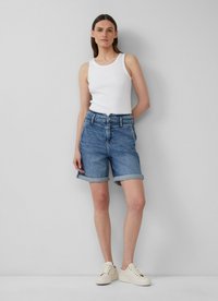 Shorts en denim bleu clair avec ourlets retroussés, taille haute, cinq poches et fermeture à bouton. Portés avec un débardeur blanc ajusté et des baskets beiges.