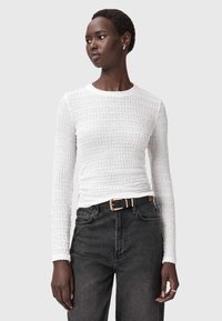 Witte langslijf-top met textuurstof en een getailleerde pasvorm, gecombineerd met hoge zwarte jeans en een zwarte riem met een gouden gesp.