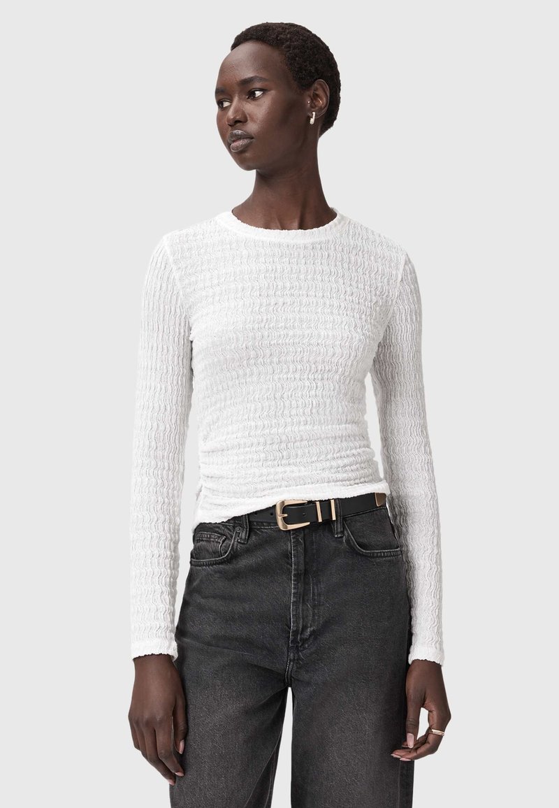 Witte langslijf-top met textuurstof en een getailleerde pasvorm, gecombineerd met hoge zwarte jeans en een zwarte riem met een gouden gesp.