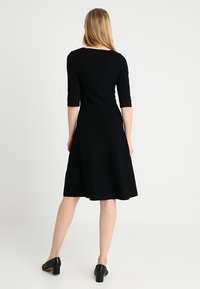 Robe noire mi-longue avec des manches courtes, texture côtelée, corsage ajusté et jupe évasée. Design simple et classique.