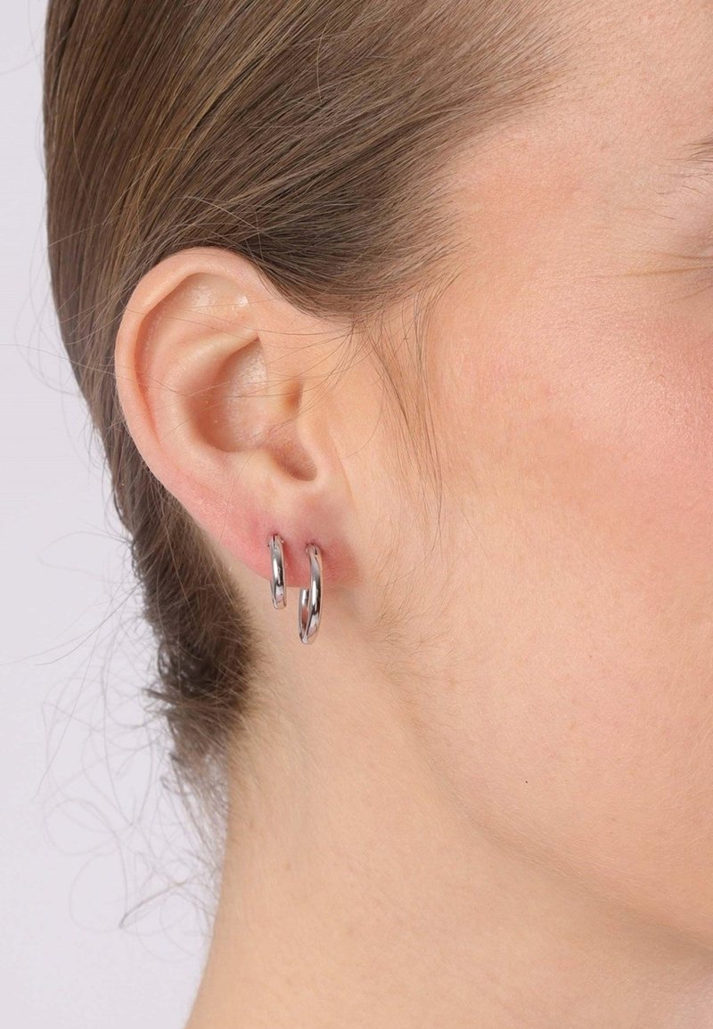 Boucles d'oreilles en argent, design circulaire, finition métal poli, deux anneaux empilés, portées dans une oreille, mettant en avant la texture lisse et la brillance.
