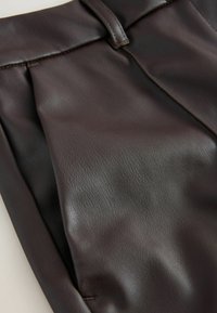 Brune læderbukser med en blød tekstur, der har folder og et glat taljeområde. Detaljeret syning langs kanterne forbedrer designet.