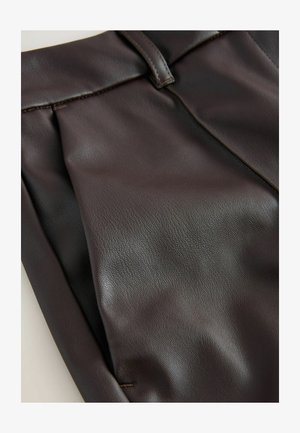 Braune Lederhosen mit weichem Material, ausgestattet mit Falten und einem glatten Bund. Detaillierte Nähte entlang der Kanten betonen das Design.