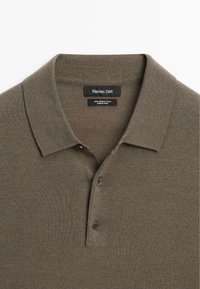 Olive green polo shirt made of 100% merino wool, featuring a soft texture, flat collar, and two dark buttons at the neckline.