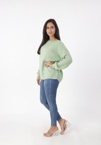 Hellgrüner, übergroßer Strickpullover mit langen Ärmeln, kombiniert mit blauen Skinny-Jeans und transparenten, hochhackigen Sandalen. Einfaches, strukturiertes Design.