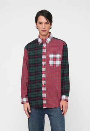 Camisa de cuadros rojos y verdes con cuello abotonado, que presenta diferentes patrones de cuadros y un bolsillo en el pecho. Hecha de tela de algodón.