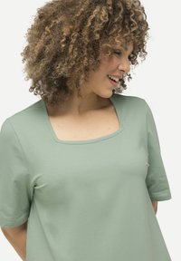 Top verde chiaro a maniche corte con scollatura quadrata, realizzato in tessuto morbido con una finitura liscia e dettagli di cucitura minimi.