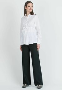 Blusa bianca con cintura a cravatta, maniche lunghe e chiusura con bottoni. Abbinata a pantaloni neri a gamba larga e scarpe a fantasia in bianco e nero.