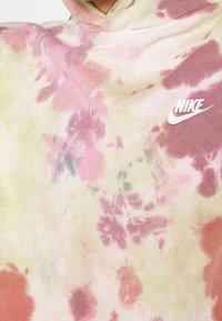 Mikina Nike s tie-dye vzorem v růžových, zelených a krémových odstínech. Bavlněný materiál s viditelnou texturou a bílým logem.