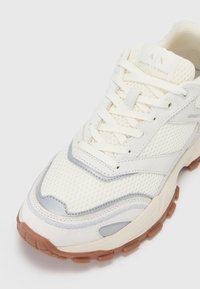 Sneaker bianca in rete e suede con accenti grigi e suola crema. Caratterizzato da lacci, tessuto testurizzato e suola in gomma. Logo del marchio sulla linguetta.