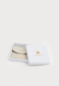Tarjetero de cuero beige dentro de una caja blanca con letras doradas. El tarjetero cuenta con un cierre a presión y una textura suave.