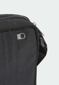 Bolsa de nylon negra con una textura suave, que presenta un cierre reluciente, un detalle de lazo lateral y un robusto sistema de sujeción en un costado.