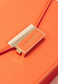 Oranžová kabátová taška z umělé kůže s obdélníkovým kovovým západkou s rytinou "ANNA FIELD". Hladký povrch s čistým prošíváním.