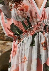 Virágmintás ruha rózsaszín és fehér színkombinációval. Átlátszó anyagból készült, smockolt derékkal és nagy virágmintákkal zöld és narancssárga árnyalatokban.