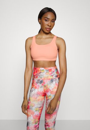 Sutiã desportivo pêssego com alças largas, combinado com leggings de cintura alta com um vibrante padrão floral em tons de rosa, laranja e cinza.