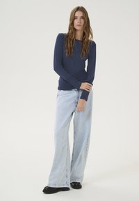 Navy long-sleeve top paired with light blue wide-leg jeans. The jeans feature a faded finish and are cuffed at the bottom, worn with black shoes.