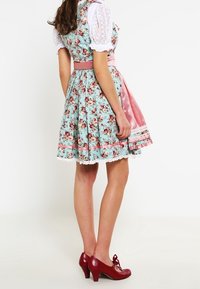 Vestido dirndl floral con una base azul claro, acentos rosas y mangas blancas abullonadas. Tacones rojos complementan el aspecto general.
