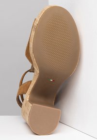 Sandalo con zeppa in suede marrone, base in sughero e suola in gomma testurizzata; presenta cinturini incrociati e una forma della punta arrotondata.