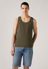 Olívazöld pamut ujjatlan póló kerek nyakkivágással és egy kis piros Levi's logóval, kék farmer sorttal párosítva. Egyszerű, laza dizájn.